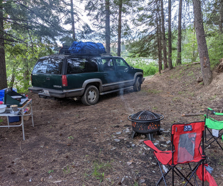 Campsite fun with an RV rental alternative: a Chevy Suburban, complete with a cozy fire pit, cooking setup, and chairs.
