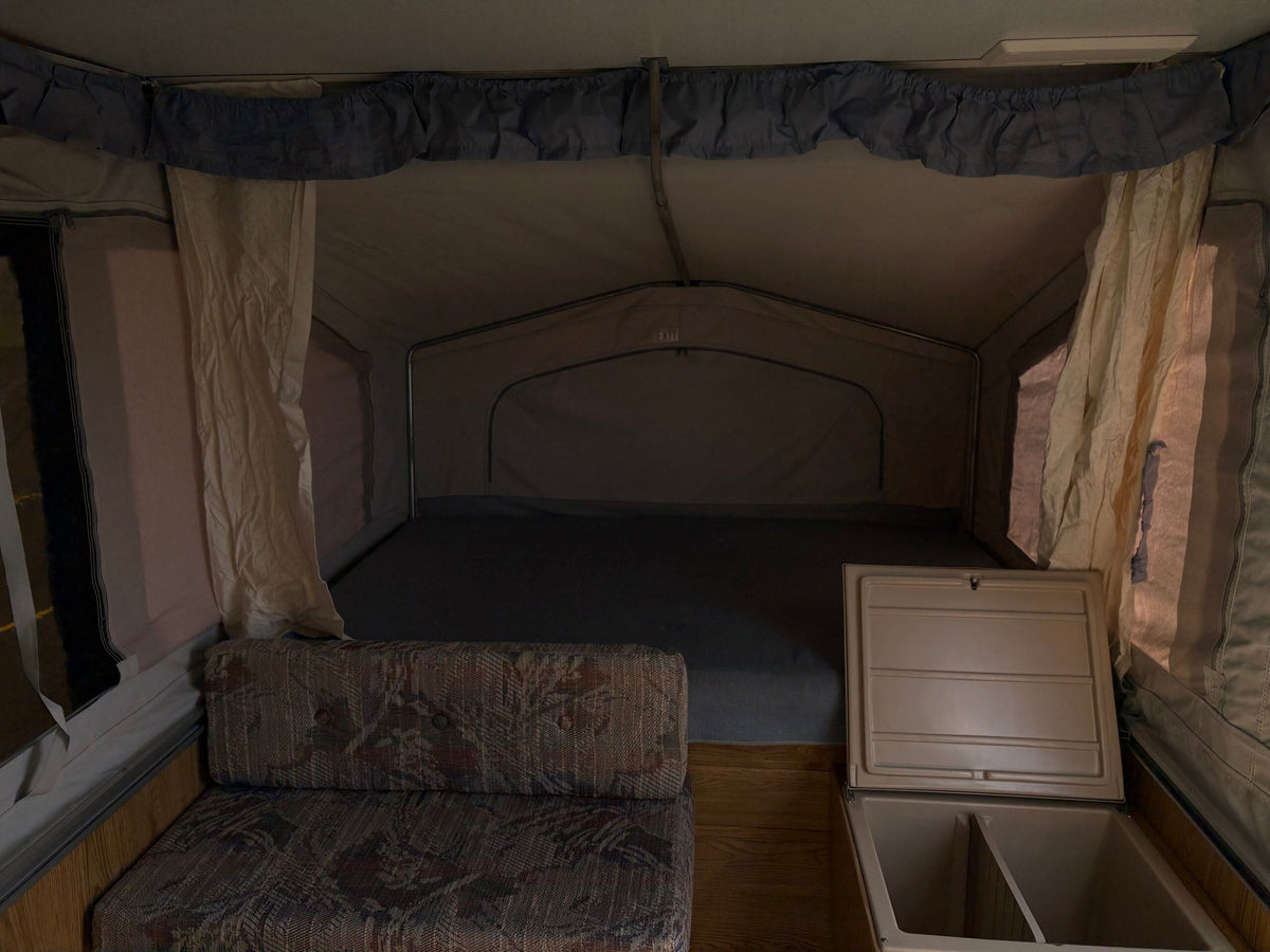 Interior of an RV rental pop-up camper with a comfy bed, couch, and cooler storage. — photo 3