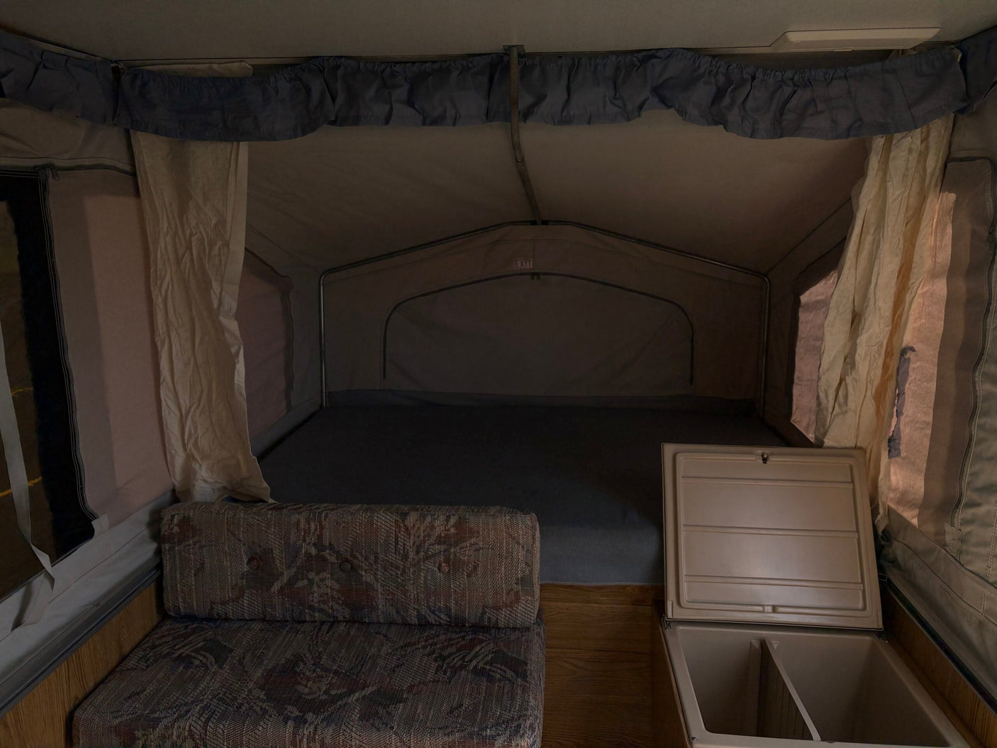 Interior of an RV rental pop-up camper with a comfy bed, couch, and cooler storage.