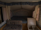 Interior of an RV rental pop-up camper with a comfy bed, couch, and cooler storage.
