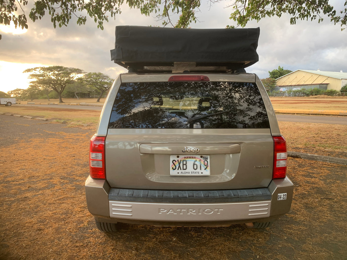 Tan Jeep Patriot with a rooftop tent in Hawaii, perfect for an RV rental adventure. License plate SXB 619.