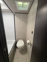 Compact RV rental bathroom featuring a shower, toilet, and modern light wood interior. Ideal for road trips.