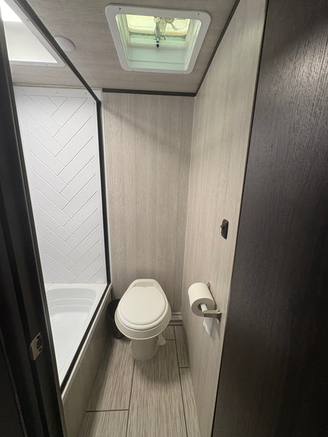 Compact RV rental bathroom featuring a shower, toilet, and modern light wood interior. Ideal for road trips.