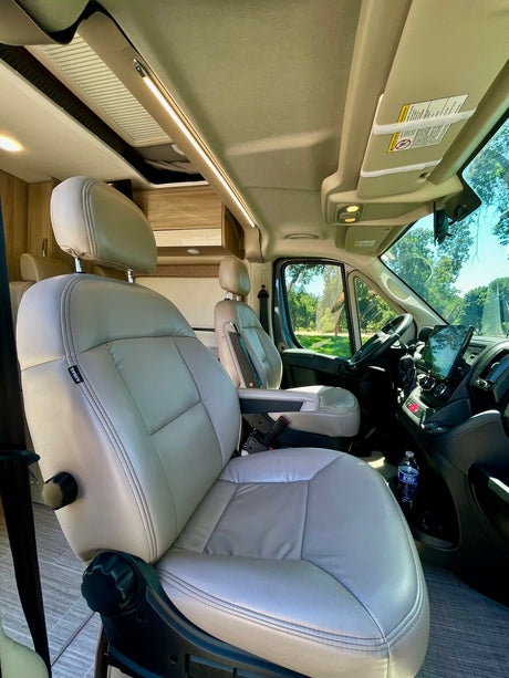 Spacious camper van RV rental interior with light leatherette seats, modern dash, and overhead lighting for travel.
