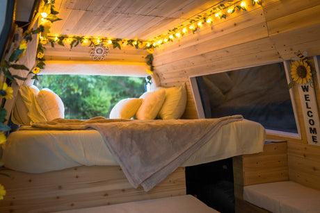 Cozy RV rental interior: bed, window view, and charming string lights on wooden walls create a welcoming retreat.