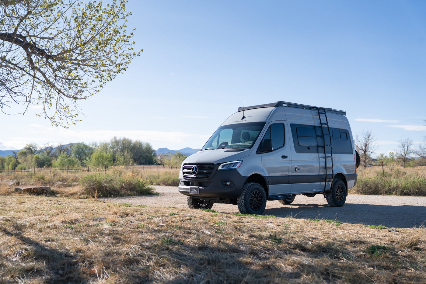 A grey Sprinter camper van, ideal for rv rental adventures, parked on a dirt path with a tree and mountains in background. — photo 6