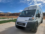 White Winnebago rv rental camper van at a scenic desert campground, featuring red rock mountains under a bright blue sky.