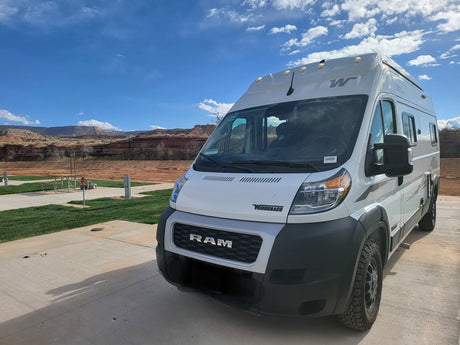 White Winnebago rv rental camper van at a scenic desert campground, featuring red rock mountains under a bright blue sky.