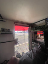 Relaxing inside an RV rental, enjoying the view of a red canopy and RV park from the open doorway. Power setup visible.