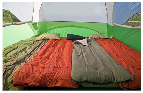 View inside a green and white tent showing three sleeping bags (orange & grey) and pillows, ready for an RV rental camping trip.