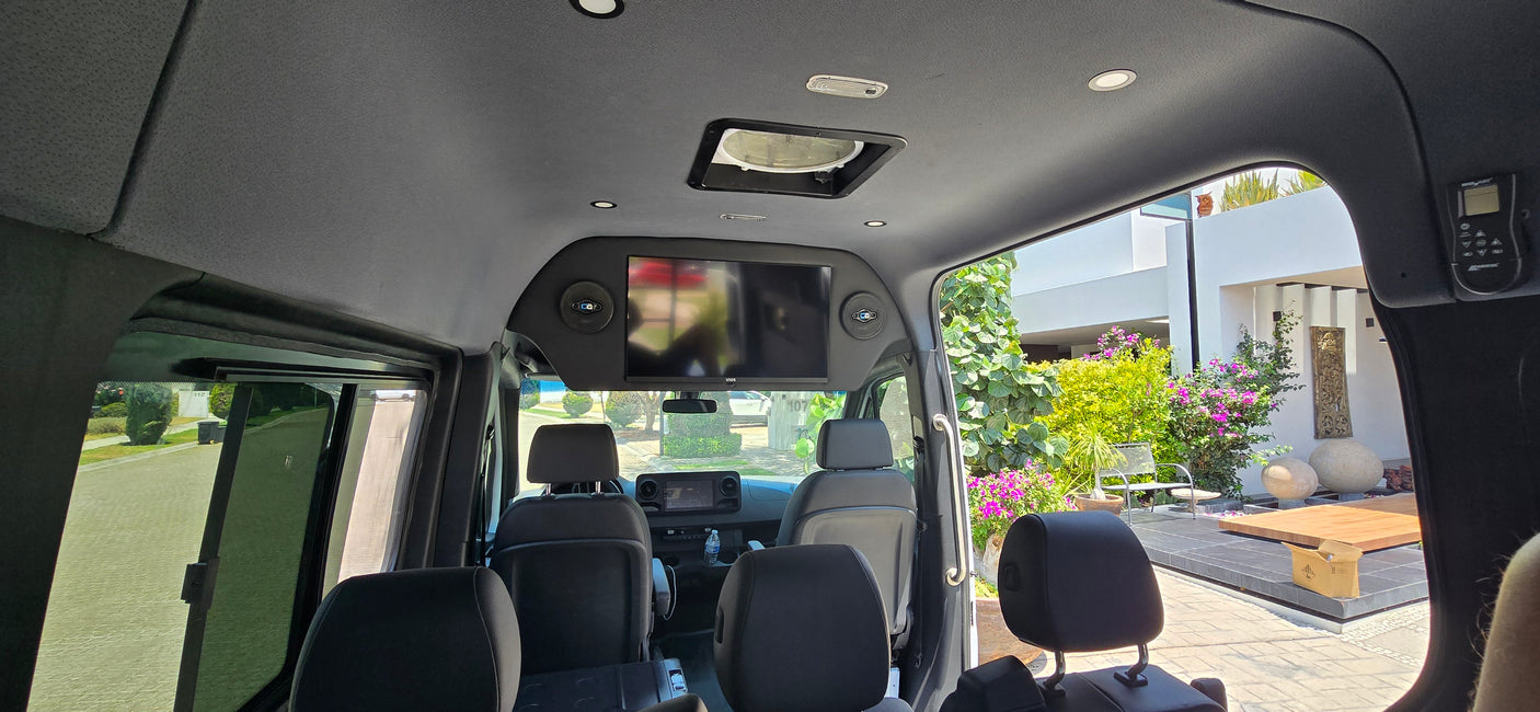 Inside a plush rv rental, revealing an overhead TV, comfy seating, and a clear view of the sunny outdoors.