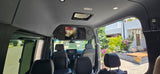 Inside a plush rv rental, revealing an overhead TV, comfy seating, and a clear view of the sunny outdoors.