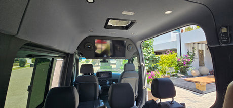 Inside a plush rv rental, revealing an overhead TV, comfy seating, and a clear view of the sunny outdoors.