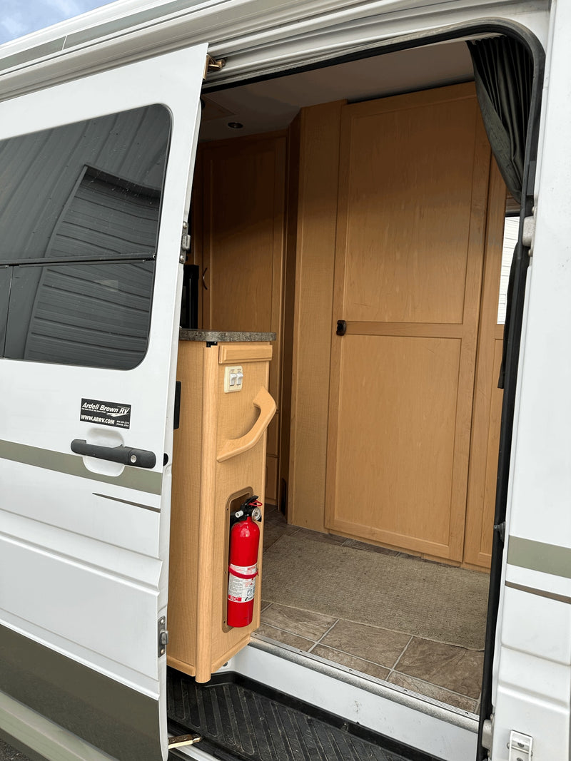 Inside an RV rental, showcasing the wood cabinetry, countertop, and a mounted fire extinguisher near the open side door. — photo 9