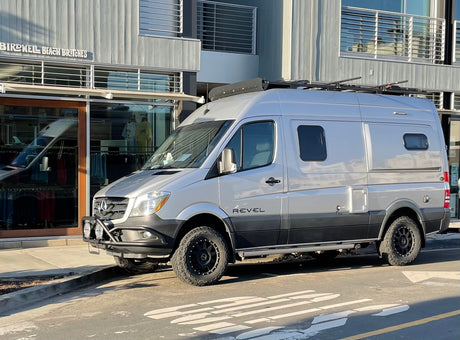 Silver Winnebago Revel Sprinter van, perfect for rv rental adventures, featuring off-road tires and roof rack.