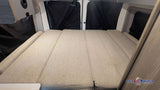 This RV rental features a folded-out bed with light-colored cushions and black privacy curtains, inside a cozy camper.
