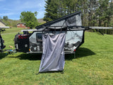 RV rental: Off-road pop-up camper trailer with privacy tent ready for adventure. Sunny day, grassy field, mountain views.