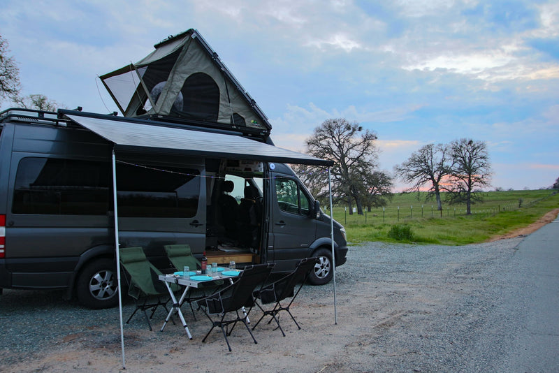  and chairs.|This RV rental offers comfort: a woman relaxes inside a camper van with an awning — photo 1