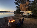 Enjoy a serene RV rental camping experience! A cozy campfire burns by a teardrop trailer and a calm lake at twilight.