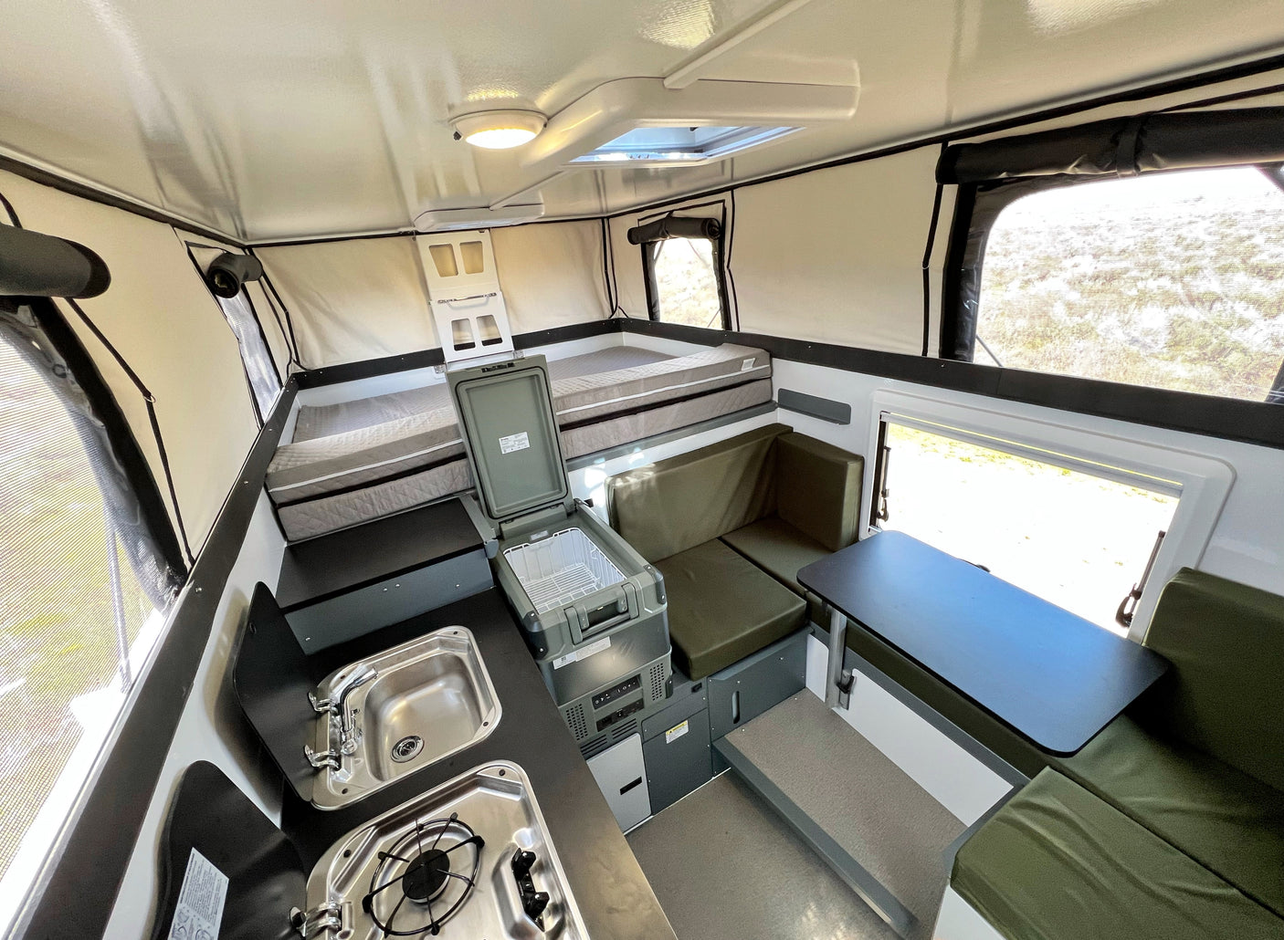 RV rental interior: comfy bed, compact kitchen with sink/stove, and dining area. Ready for adventure!