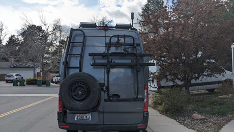 Rear view of an RV rental Mercedes Sprinter camper van, equipped with bike rack, ladder, and roof solar panels.