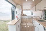This RV rental offers a well-designed camper van interior with a bed, kitchen, and open views of the beach & sea.
