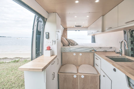 This RV rental offers a well-designed camper van interior with a bed, kitchen, and open views of the beach & sea.