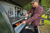 Man using an RV rental's compact outdoor kitchen with sink, stove, and storage. Perfect for camping adventures!