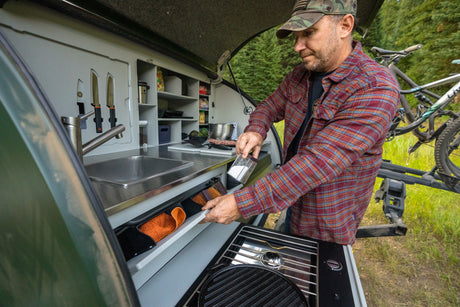 Man using an RV rental's compact outdoor kitchen with sink, stove, and storage. Perfect for camping adventures!