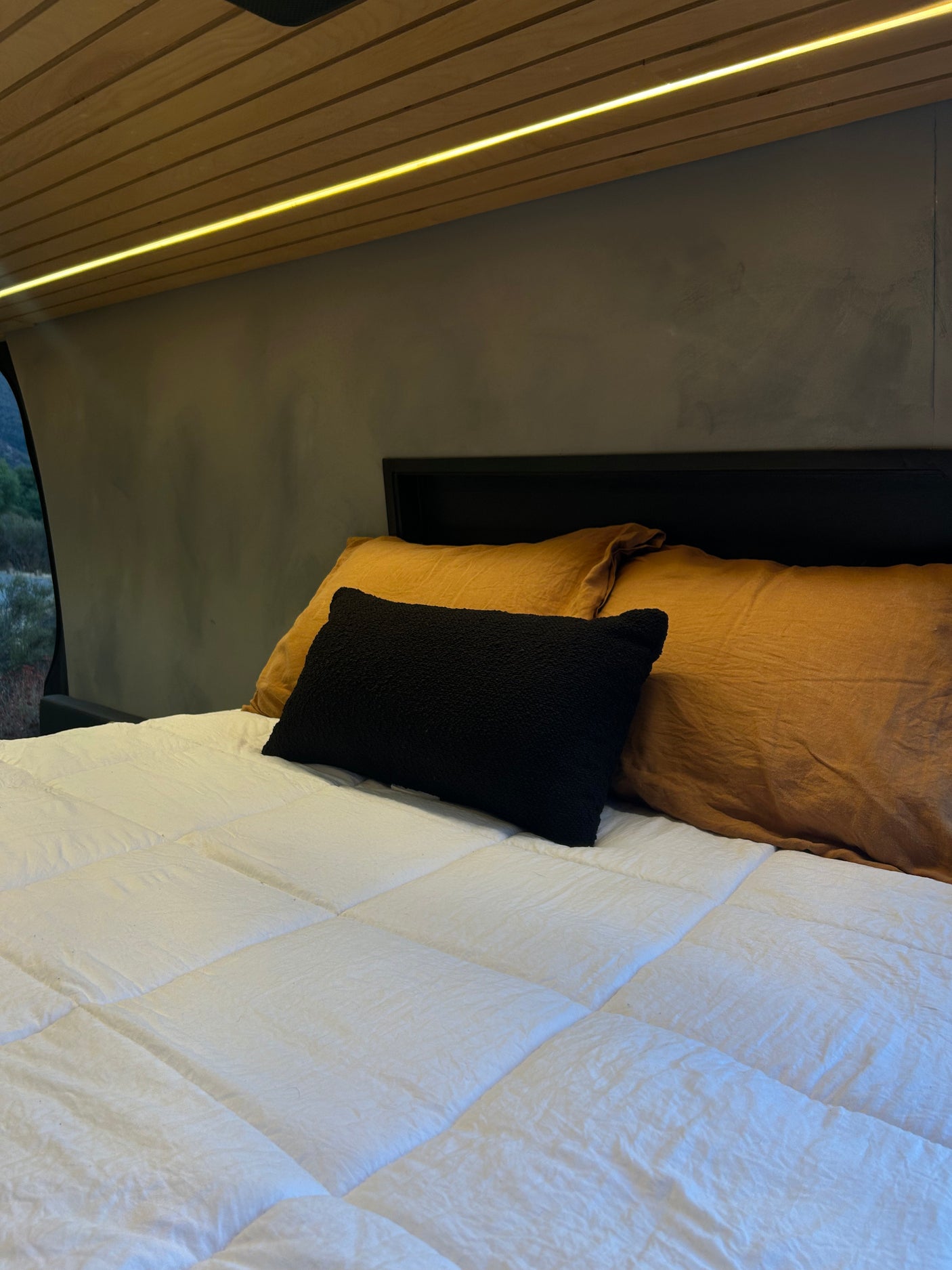 A well-made bed with a white comforter and golden pillows inside an RV rental, featuring a sleek lighted wood ceiling.