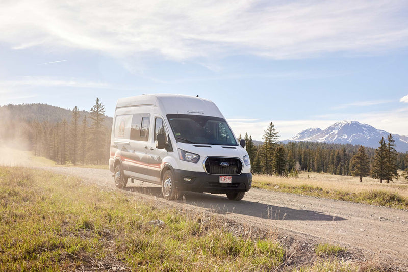  overlooking a valley town. Perfect for a scenic road trip.|This white Ford Transit rv rental camper van drives a dusty mountain road — photo 4