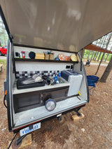 Outdoor kitchen of a small rv rental trailer, fully equipped with sink, fridge, and griddle for comfortable camping.