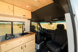 Inside this RV rental: a custom wood kitchen with sink, stove, & cabin view. Desert landscape outside.