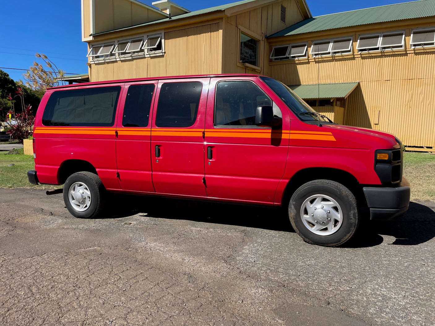 Vibrant red van with orange stripes, a spacious RV rental option, parked on asphalt near a large building.