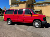 Vibrant red van with orange stripes, a spacious RV rental option, parked on asphalt near a large building.