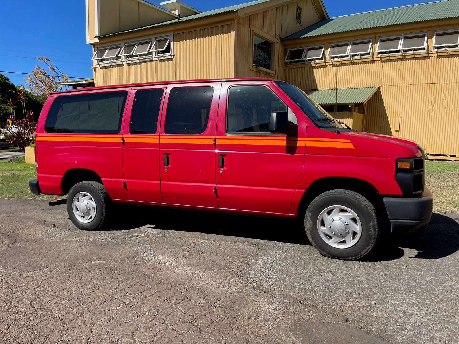 Vibrant red van with orange stripes, a spacious RV rental option, parked on asphalt near a large building.