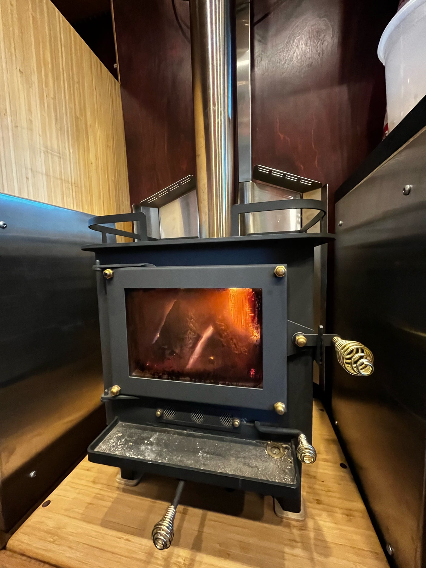 A compact black wood stove with glowing logs inside, featuring a metal flue and heat shields, perfect for a cozy RV rental.