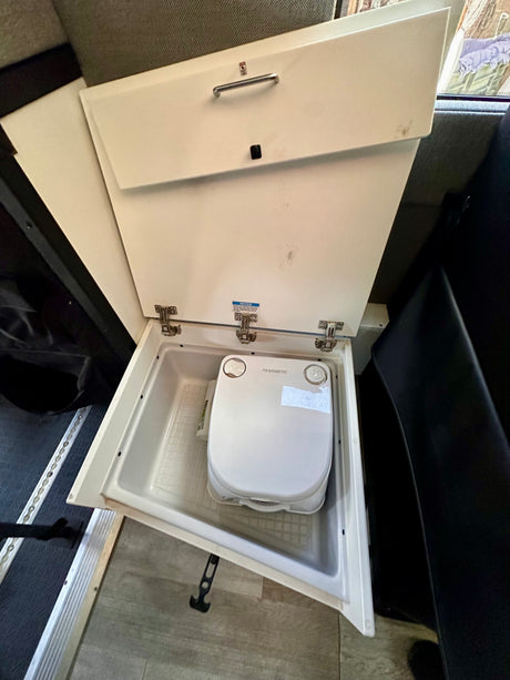 A compact Dometic portable toilet, neatly stored in a hidden compartment, ideal for an RV rental.