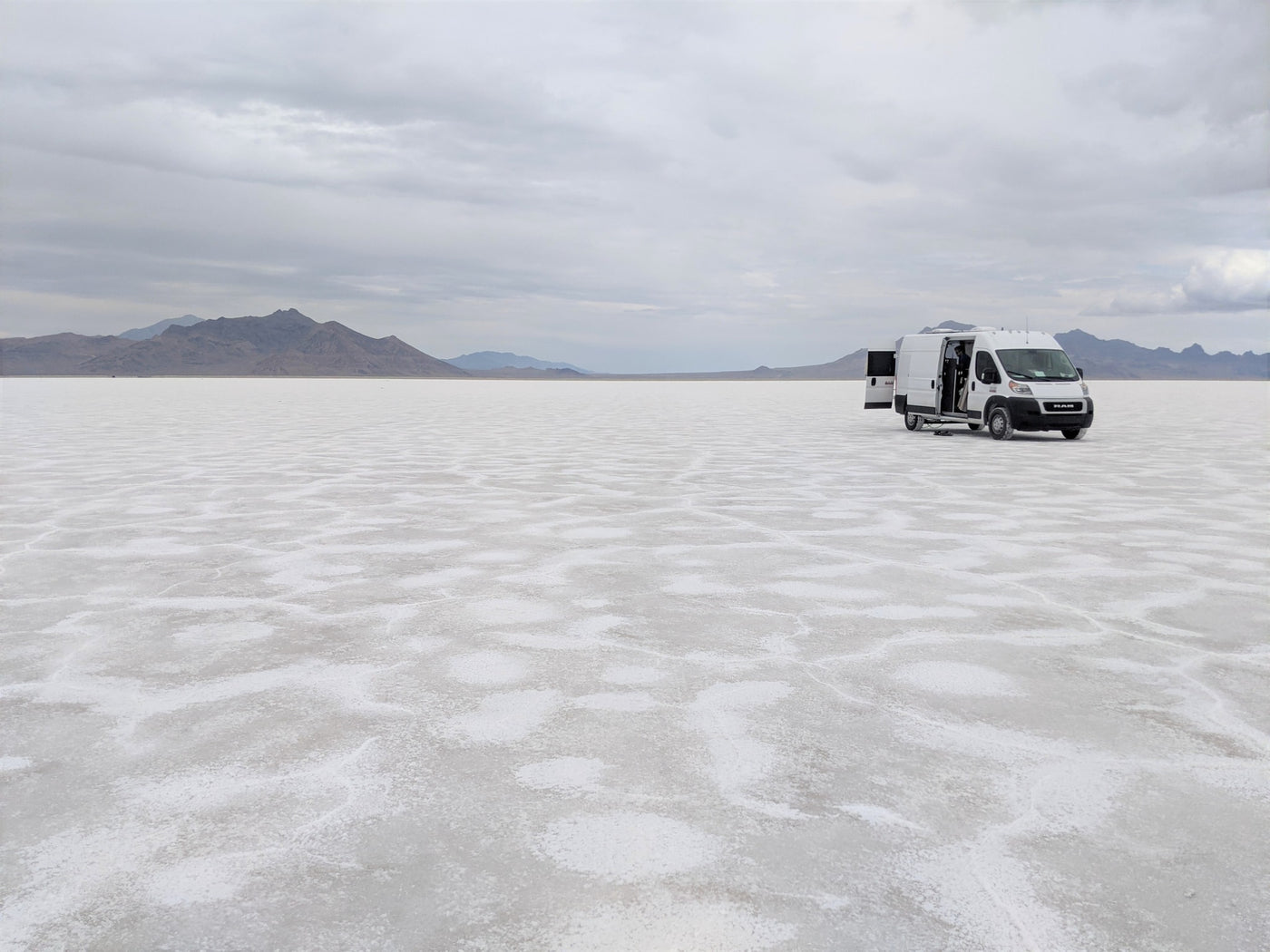  overlooking a vast lake and hills under a sunny sky.|White RV rental van on vast Bonneville Salt Flats with open doors — photo 2