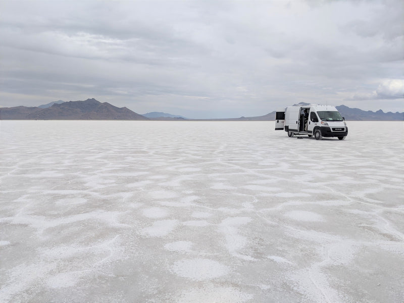  overlooking a vast lake and hills under a sunny sky.|White RV rental van on vast Bonneville Salt Flats with open doors — photo 2