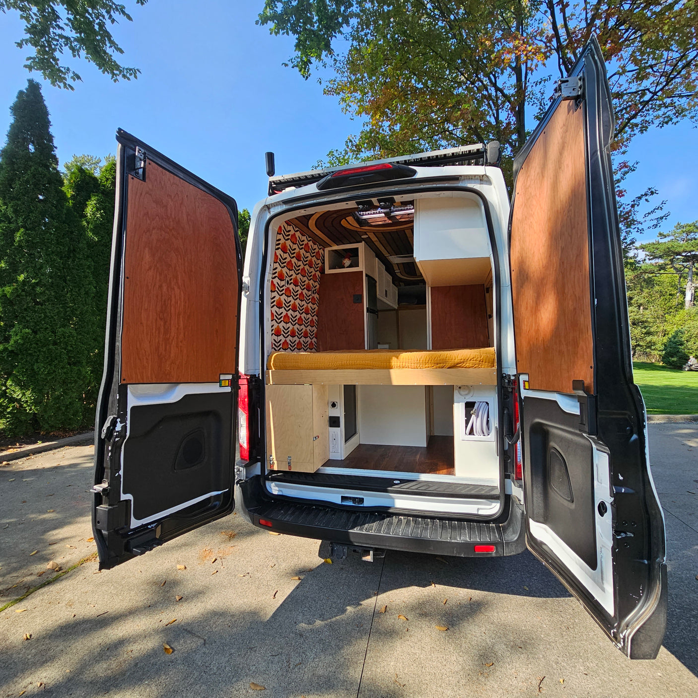 Ready for adventure: This RV rental camper van showcases its custom interior, with rear doors open revealing a bed and wood accents.