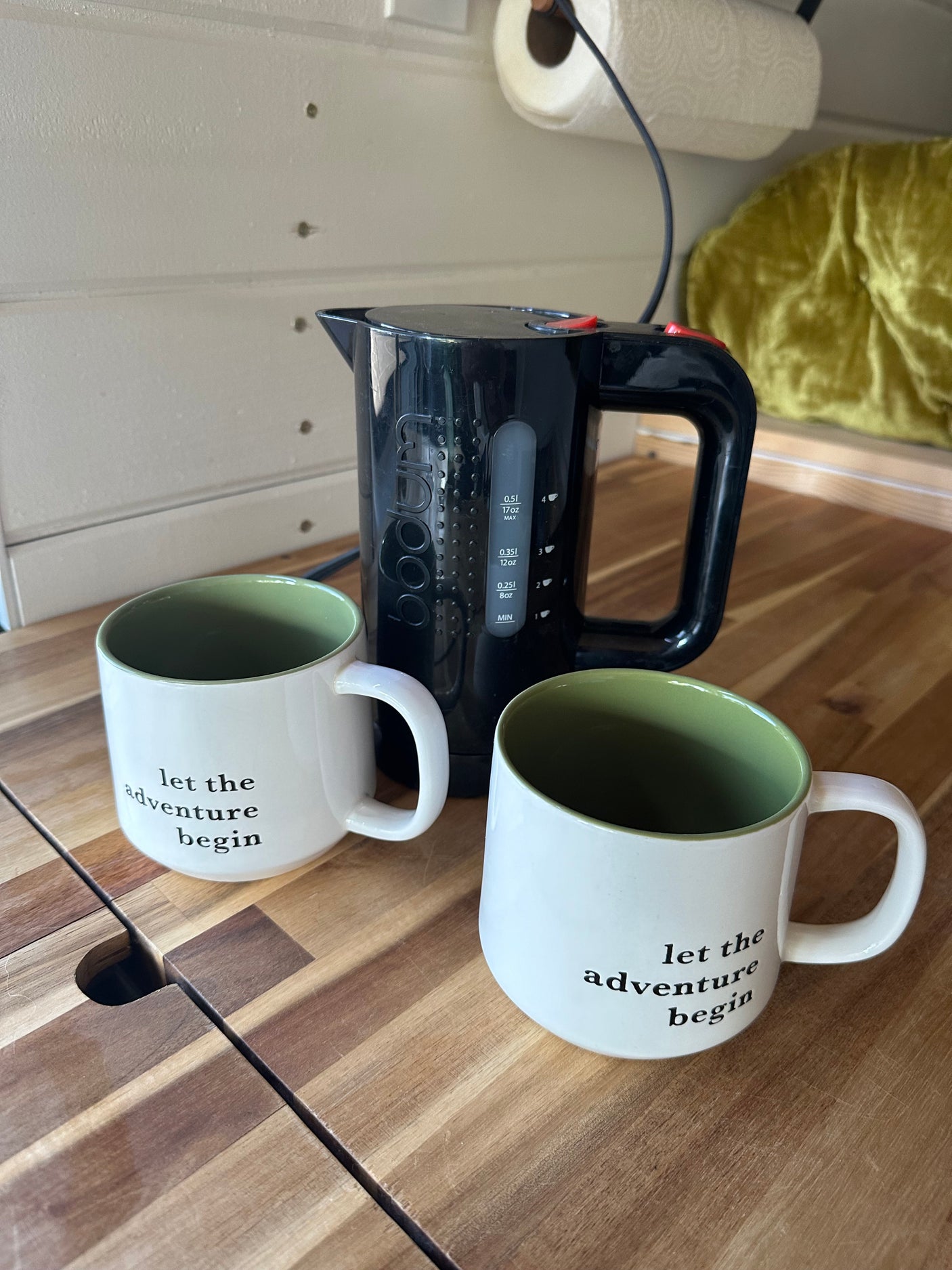 Start your day with coffee in your RV rental! Black kettle & 'let the adventure begin' mugs on a wood counter.