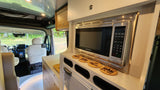 Modern **RV rental** kitchen with a Contoure microwave, counter, "Up North" coasters, and view of the front cabin.
