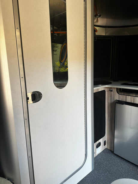 RV rental interior: View from a door with a reflective panel into a compact kitchen with a fridge and counter.
