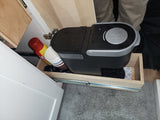 Compact coffee station with supplies on a pull-out tray inside an RV rental cabinet.