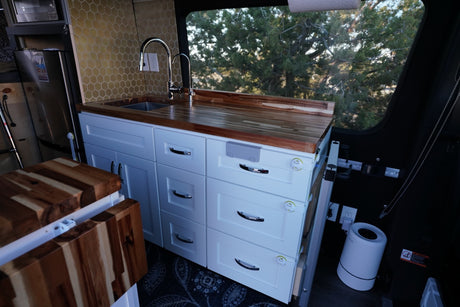 Custom RV rental kitchen featuring white cabinets, wood counters, hexagonal backsplash, and child-proof drawer latches.