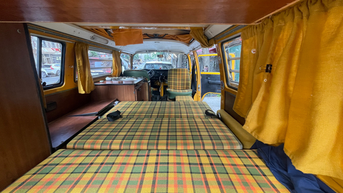 Experience a cozy RV rental: vintage camper interior with plaid bed, compact kitchen, & driver's view.