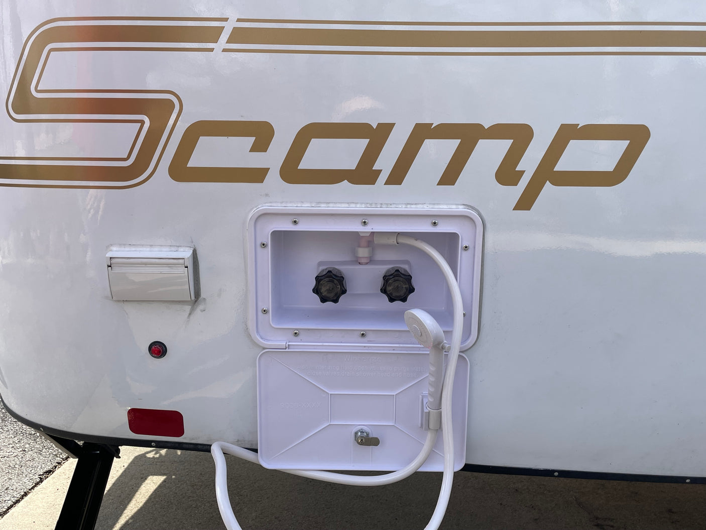 Exterior of a white Scamp RV rental, showing its open panel with a hot/cold outdoor shower.