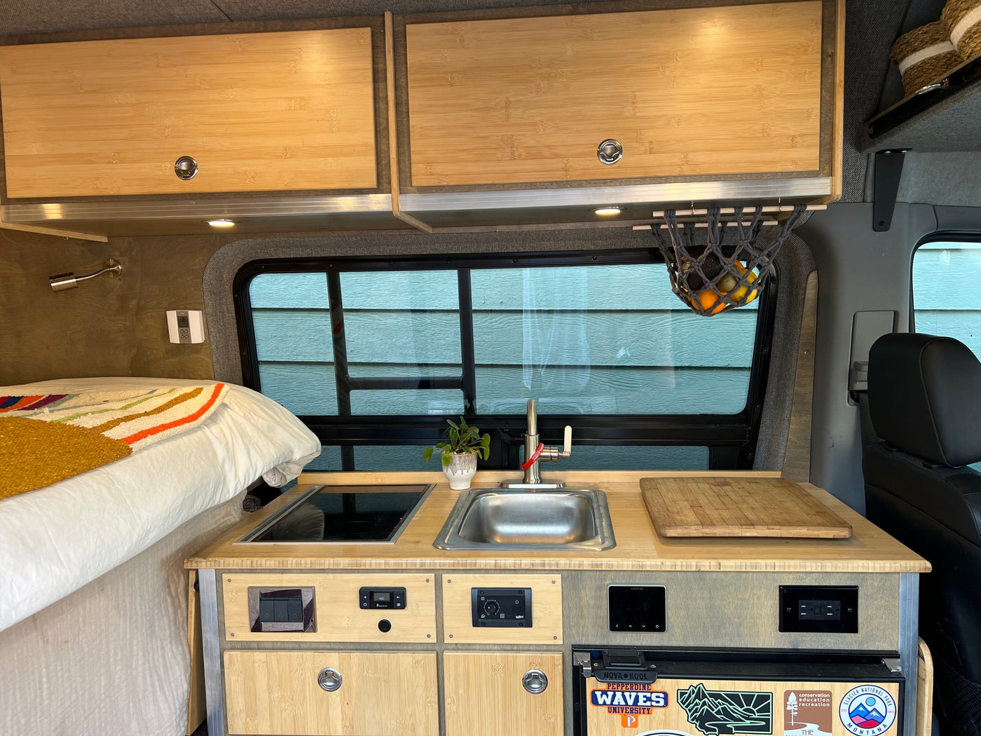 Compact RV rental interior featuring a bamboo kitchen, sink, cooktop, and cozy bed area, perfect for mobile adventures. — photo 10