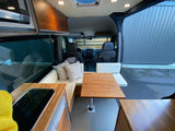 Camper van RV rental interior: a U-shaped dinette with wood table, kitchenette, and overhead cabinets, looking toward the front seats.